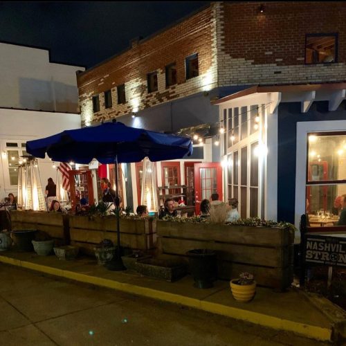 Cozy outdoor dining area at night, featuring string lights, umbrellas, and patrons enjoying their meals.