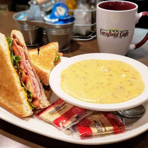A sandwich with ham and lettuce beside a bowl of creamy soup, with a coffee mug in the background.