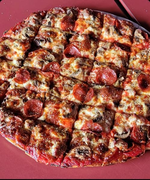 A square pizza topped with pepperoni, mushrooms, and melted cheese, cut into even slices on a red plate.