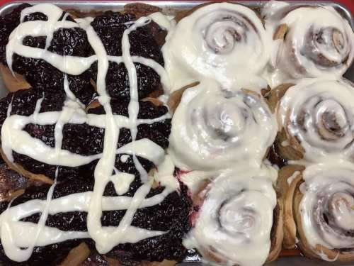 A tray of cinnamon rolls drizzled with icing, alongside pastries filled with dark berry jam.