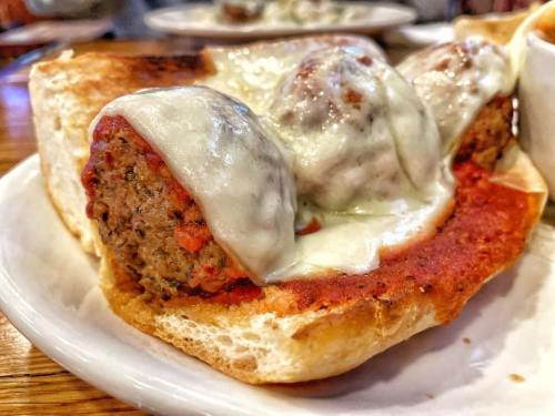 A close-up of a meatball sandwich topped with melted cheese and marinara sauce on a toasted roll.