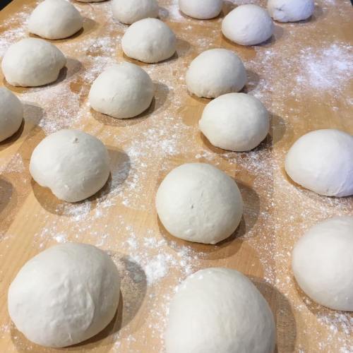 A wooden surface covered with flour, featuring multiple round dough balls ready for baking.