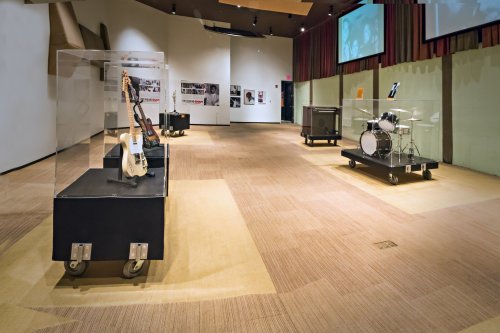 An empty exhibition space featuring display cases with a guitar and a drum set, showcasing musical instruments.
