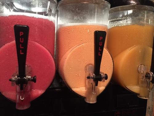Three beverage dispensers filled with colorful slushy drinks: pink, orange, and yellow, each with a "PULL" tap.