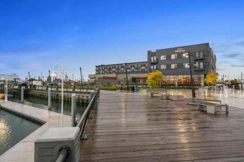 A waterfront view featuring a wooden dock, a hotel, and colorful trees under a clear blue sky.
