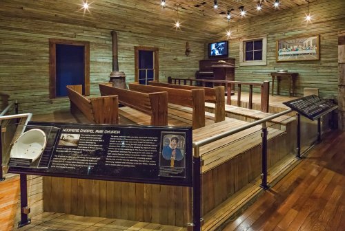 Interior of a historic church with wooden benches, a stove, and informational displays in a rustic setting.