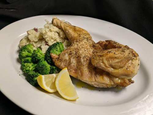 A plate featuring roasted chicken, mashed potatoes, steamed broccoli, and lemon wedges.