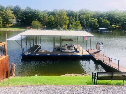 A dock with a covered boat slip on a calm lake, surrounded by trees and a grassy area.