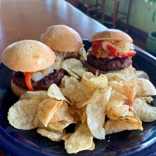 Three mini burgers with toppings on a plate, accompanied by a side of crispy potato chips.