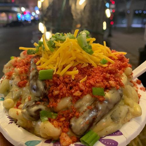 A plate of macaroni and cheese topped with crumbled snacks, shredded cheese, and green onions, served in a festive paper plate.