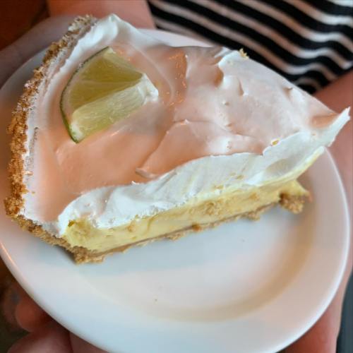 A slice of key lime pie topped with whipped cream and a lime wedge, served on a small white plate.