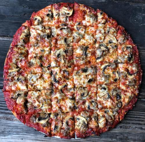 A round pizza topped with cheese, mushrooms, and sausage, cut into square slices on a wooden table.
