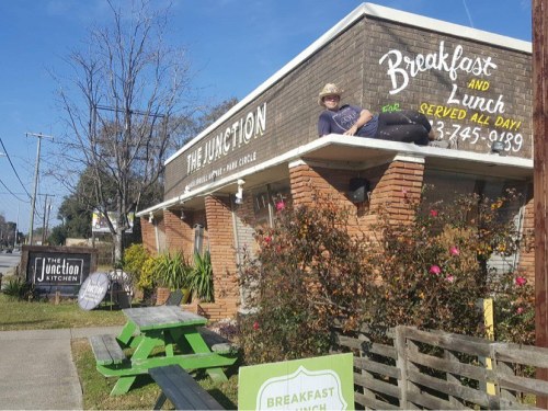 A man lounging on the roof of a restaurant called "The Junction," surrounded by greenery and outdoor seating.