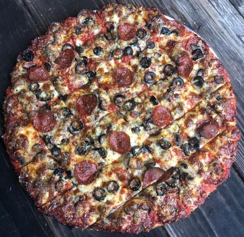 A round pizza topped with pepperoni, black olives, and melted cheese, sliced into equal pieces on a wooden surface.