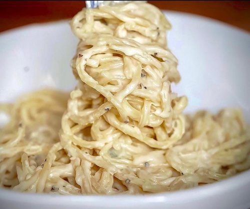 A fork twirls creamy spaghetti in a white bowl, showcasing a rich, cheesy sauce.
