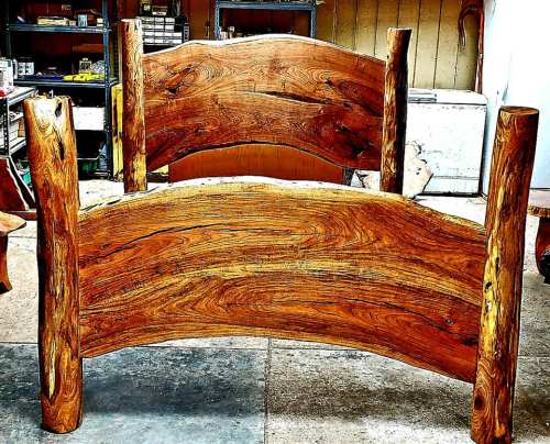 A rustic wooden bed frame with a curved headboard and footboard, featuring natural wood grain and sturdy log posts.