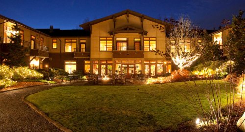 A beautifully lit building at night, surrounded by a garden with festive lights and a clear blue sky.