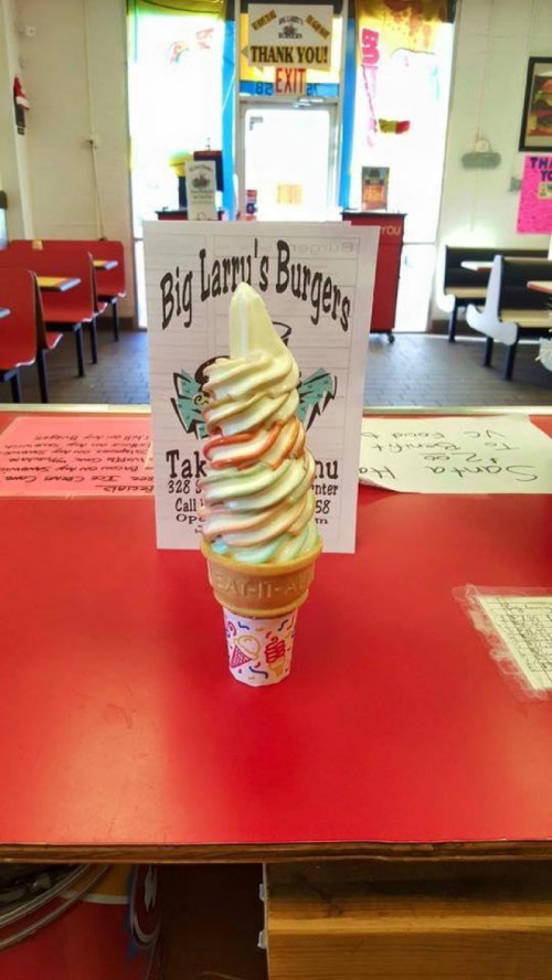 A colorful soft serve ice cream cone on a red counter, with a menu sign in the background at a burger restaurant.