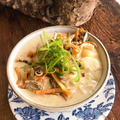 A bowl of creamy soup topped with green onions and crispy fried noodles, served on a floral-patterned plate.