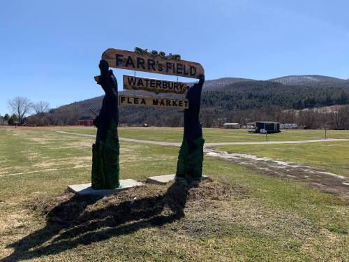 Sign for Farr's Field Waterbury Flea Market, set against a backdrop of green fields and distant mountains.