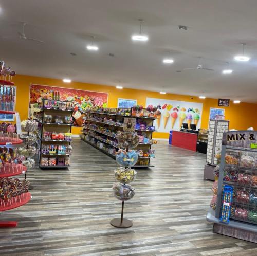 Brightly lit candy store interior with colorful shelves of sweets, lollipops, and a vibrant ice cream mural on the wall.