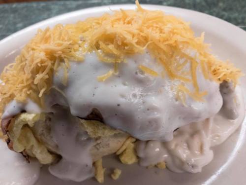 A plate of biscuits topped with creamy gravy and shredded cheese.