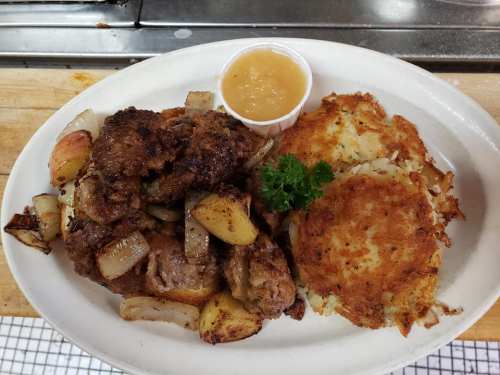 A plate of fried chicken with potatoes and onions, served with applesauce and a crispy hash brown.