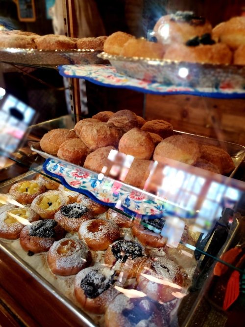 A display case filled with various pastries, including donuts and fruit-topped treats, behind glass.