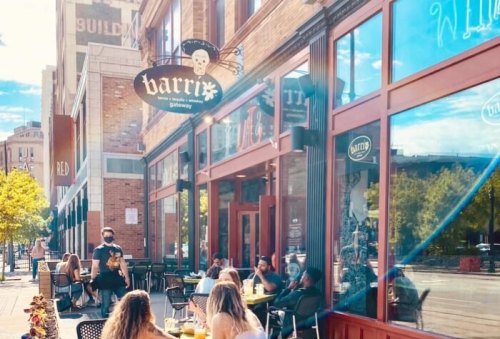 A sunny street scene featuring a restaurant with outdoor seating and people enjoying their meals.