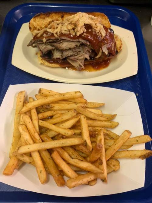 A plate with a barbecue beef sandwich topped with sauce and crispy onions, alongside a serving of golden French fries.
