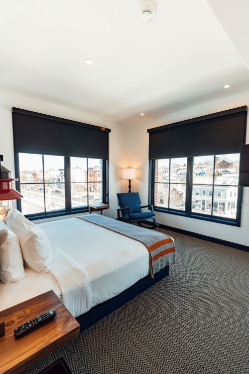 A modern hotel room featuring a bed, armchair, and large windows with city views.