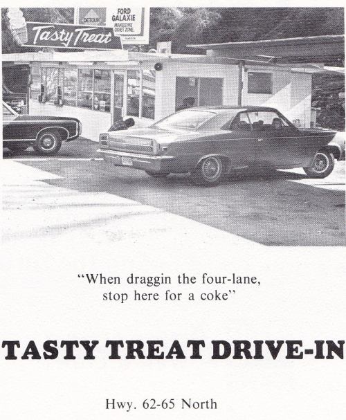 A vintage drive-in restaurant with a sign reading "Tasty Treat," featuring cars parked outside on a highway.