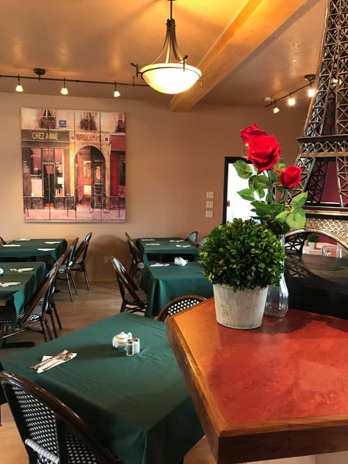 Cozy restaurant interior with green tables, a floral centerpiece, and a Parisian-themed wall art.