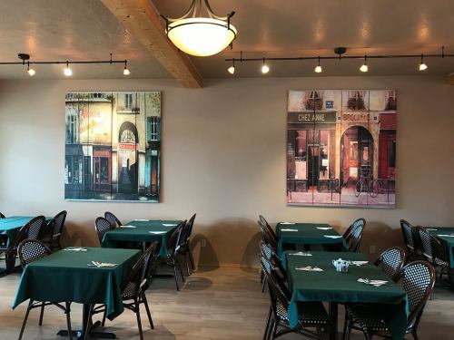 Interior of a restaurant featuring green tables and two large paintings of storefronts on the walls.