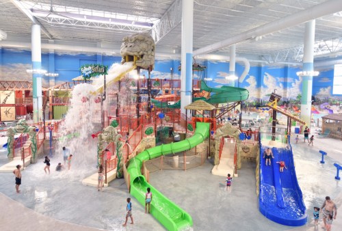 A vibrant indoor water park featuring slides, a wave pool, and children playing in a tropical-themed environment.