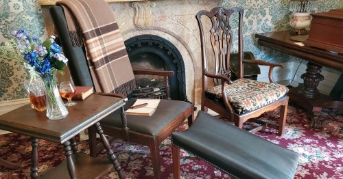 A cozy room with two chairs, a small table, a fireplace, and a vase of flowers, creating a warm, inviting atmosphere.