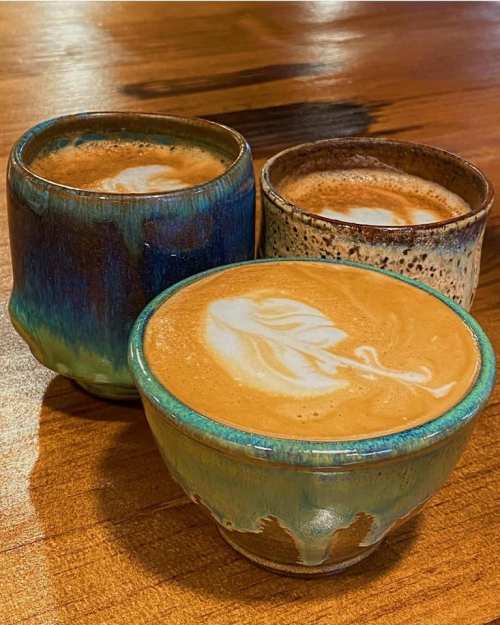Three beautifully crafted ceramic cups filled with latte art, resting on a wooden table.