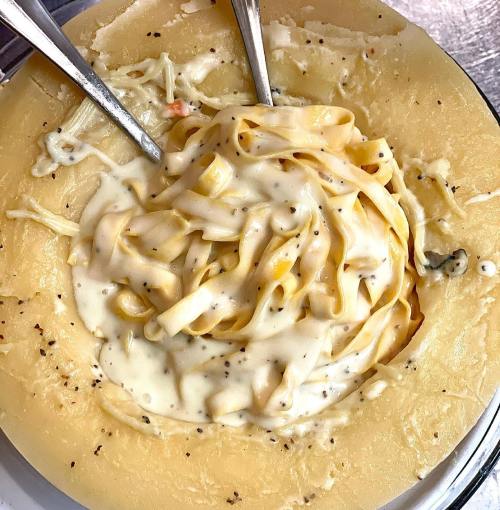 Creamy fettuccine pasta served in a hollowed-out cheese wheel, garnished with black pepper.