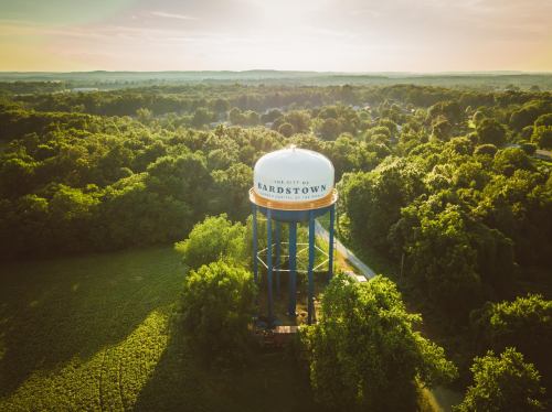 Aerial view of Bardstown water tower surrounded by lush greenery and rolling hills under a sunset sky.