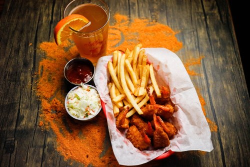 A basket of fried shrimp and fries with coleslaw and dipping sauce, alongside a drink with an orange slice.