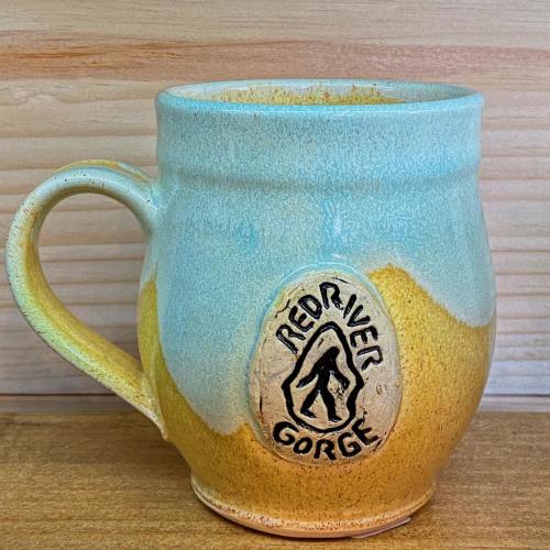 A ceramic mug with a gradient of blue and yellow, featuring a "Red River Gorge" emblem on the front.