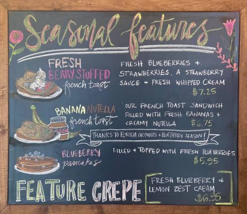 Chalkboard menu featuring seasonal dishes: berry stuffed French toast, banana Nutella French toast, blueberry pancakes, and crepes.
