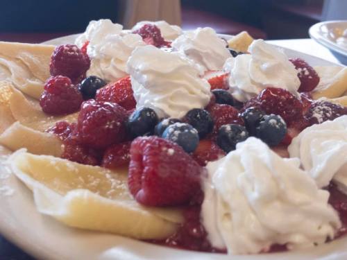 A plate of crepes topped with fresh raspberries, strawberries, blueberries, and whipped cream.