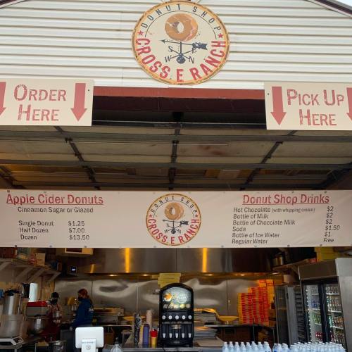 A donut shop menu displaying prices for apple cider donuts and drinks, with order and pickup signs.