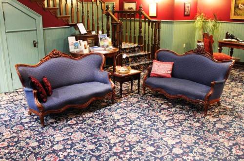 Two vintage blue upholstered sofas with ornate wooden frames, placed on a patterned carpet in a warmly lit room.