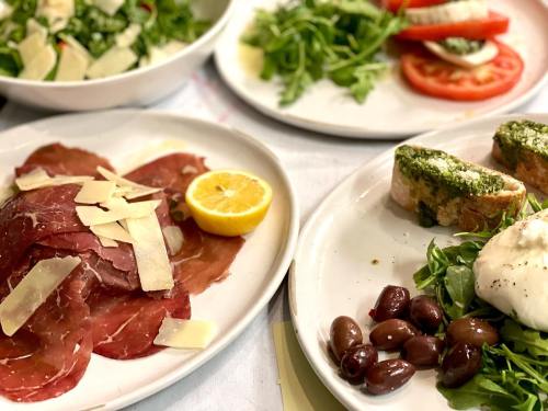 A spread of fresh dishes including cured meats, salad, olives, and bruschetta with pesto and cheese on white plates.