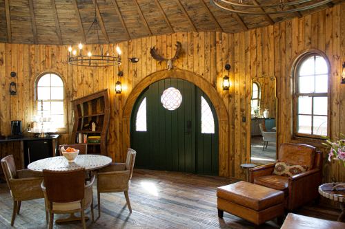 Cozy interior of a round wooden room with a green door, circular windows, and rustic furniture.
