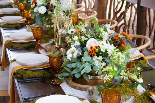 A beautifully arranged dining table with floral centerpieces, amber glassware, and natural decor elements.