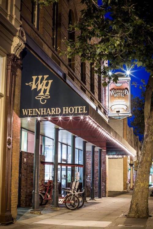 Exterior of the Weinhard Hotel at night, featuring a sign and vintage bicycles near the entrance.
