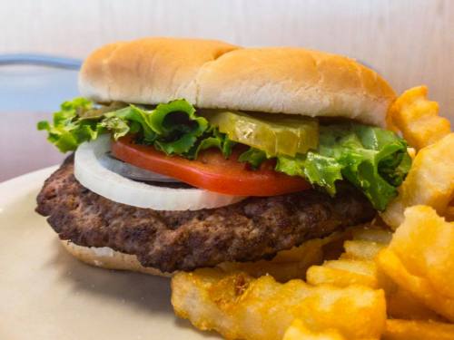 A close-up of a hamburger with lettuce, tomato, onion, and pickles, served with crinkle-cut fries on the side.